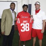Three men gathered, one holding a red jersey that says Jones 38