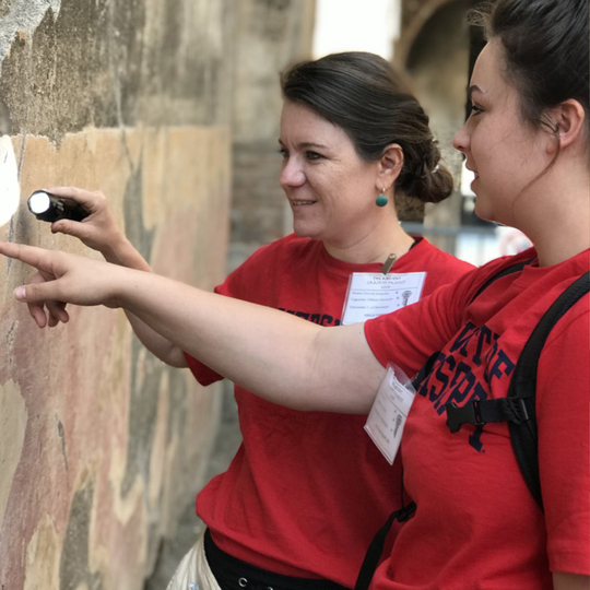 Jacqueline DiBiasie-Sammons (left) and Ole Miss student Anne Acevedo search a wall for traces of ancient graffiti using a flashlight during a trip to Pompeii in 2019