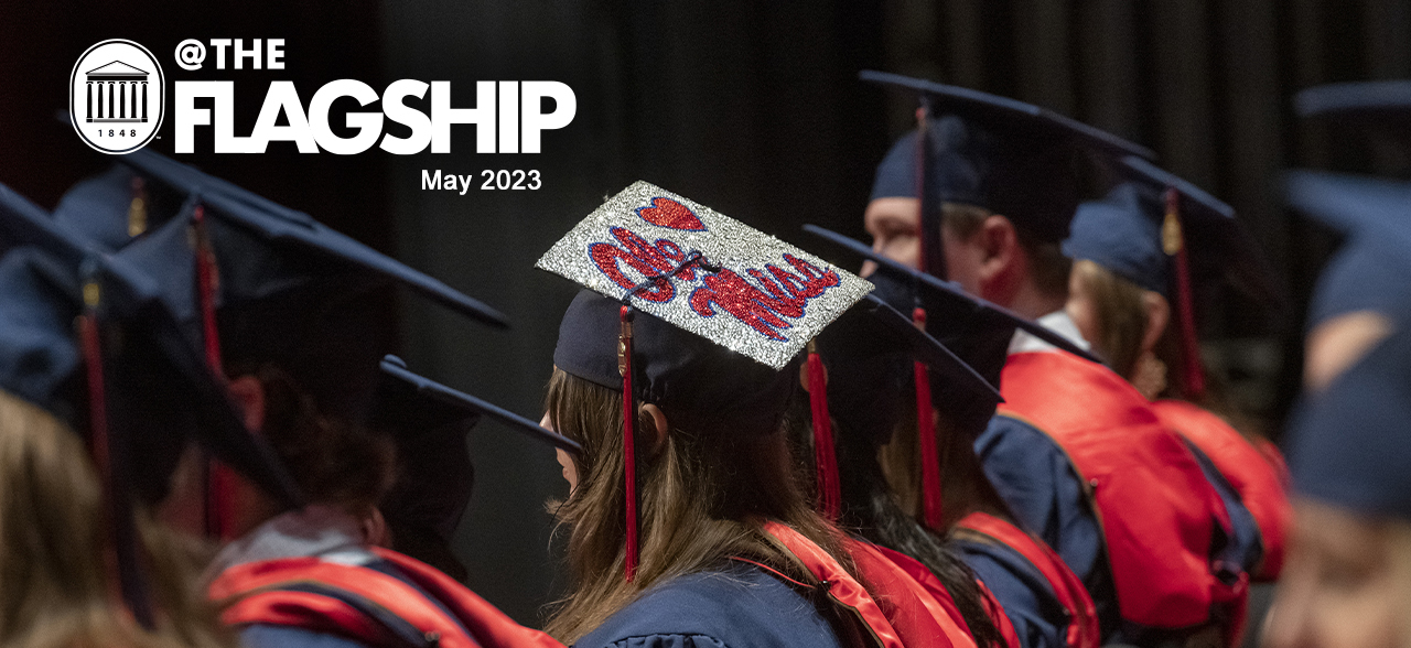 @TheFlagship May 2023. A group of graduates sit in their blue and red graduation regalia with one student wearing a cap decorated in silver with a red heart and the “Ole Miss” script on it.